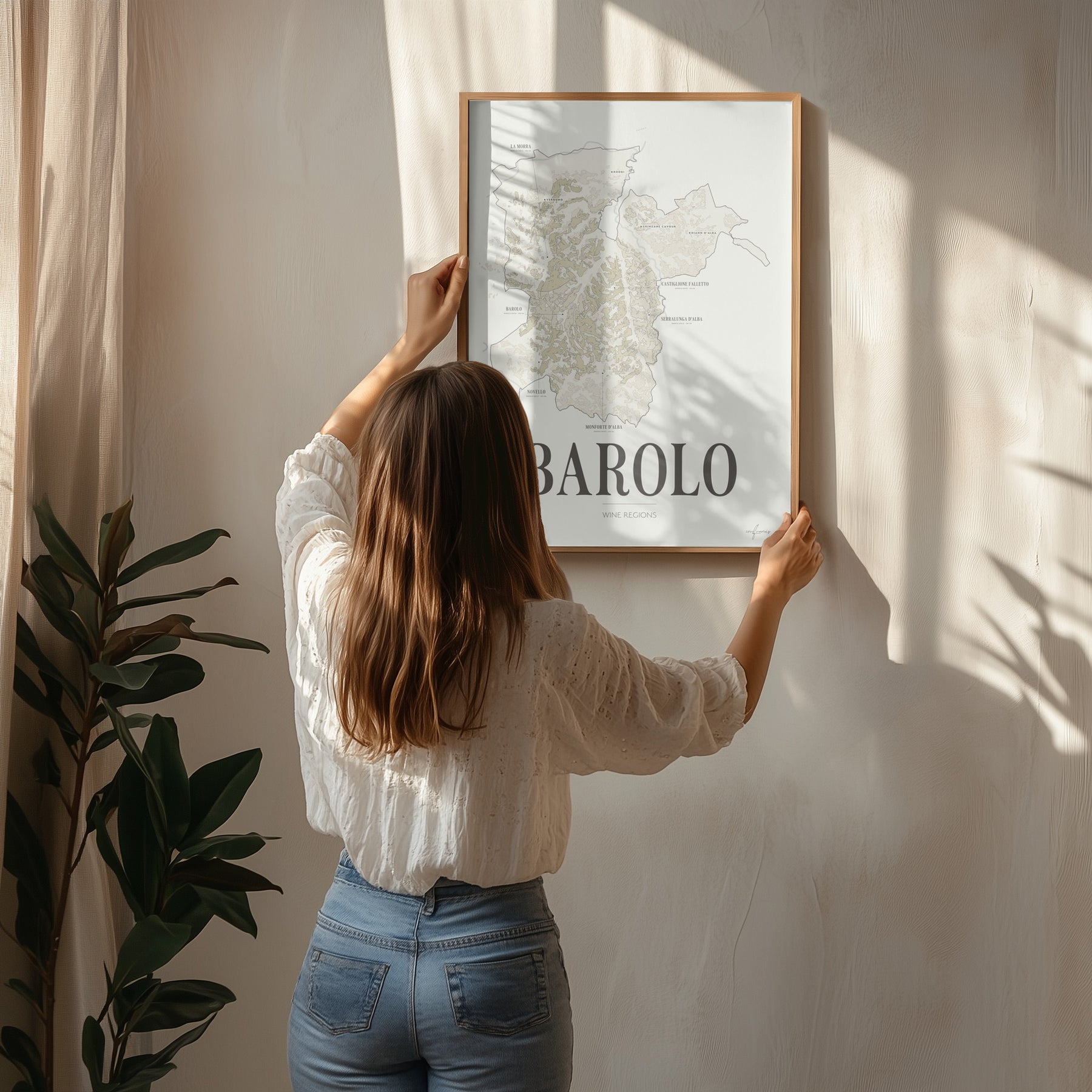 A woman hanging the framed Barolo Wine Map poster by Corkframes on a wall