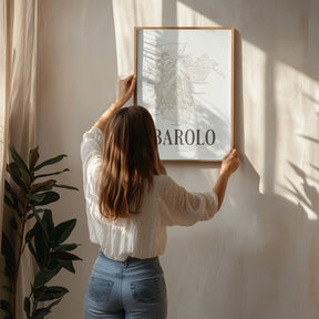 A woman hanging the framed Barolo Wine Map poster by Corkframes on a wall