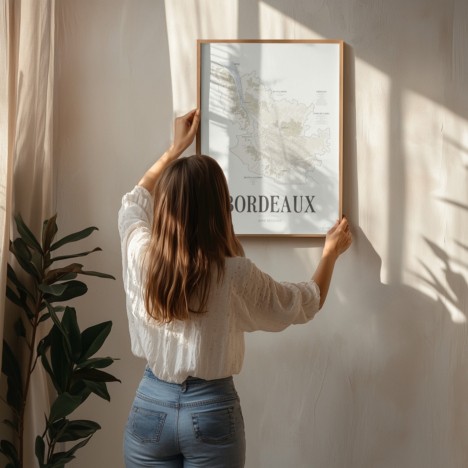 A woman hanging the framed Bordeaux Wine Map poster by Corkframes on a wall