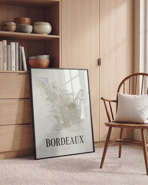 Bordeaux Wine Map poster by Corkframes in a frame leaning against a wooden wall beside a chair with a cushion
