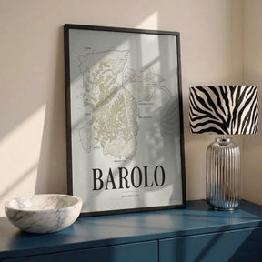 Barolo Wine Map poster by Corkframes in a black frame on a blue sideboard with a marble bowl and a striped lamp