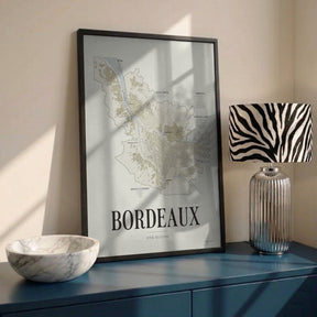 Bordeaux Wine Map poster by Corkframes in a black frame, leaning on a blue sideboard beside a marble bowl