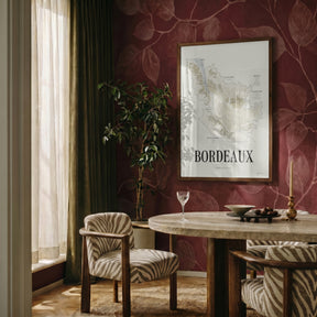 Bordeaux Wine Map poster by Corkframes framed on a deep red patterned wall in a dining room with a wine glass